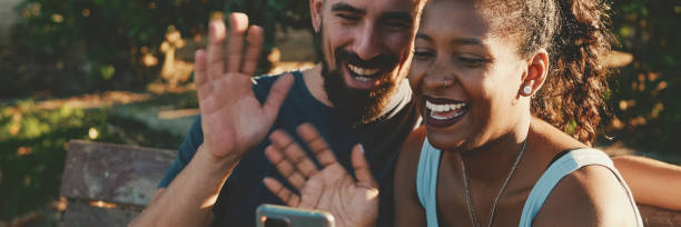 istock Happy smiling interracial couple taking selfie on phone while sitting on park bench, Panorama. 1970247962