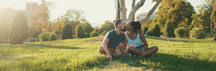 Happy smiling interracial couple talking while sitting on the grass in the park, Backlight, Panorama