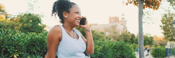 istock Laughing young mixed race woman sitting on park bench talking on cellphone, Panorama 1970257049