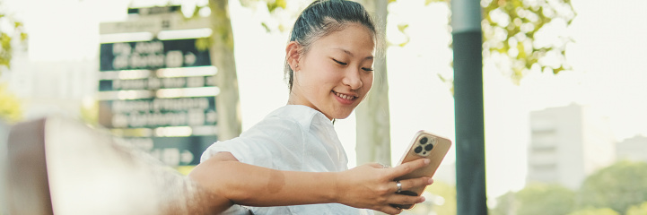Young woman sitting on bench and using mobile phone, Panorama