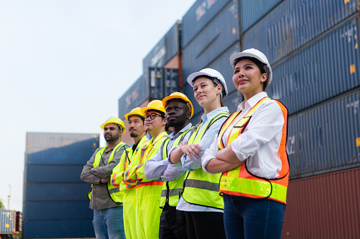 Group of worker wearing safety helmet and reflective vest standing in front of containers.