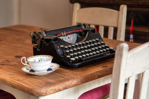old black typewriter on a vintage wooden table at home , coffee cup in the foreground