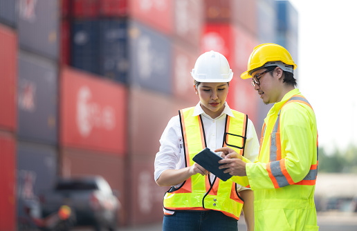 Portrait of Asian woman engineer and worker working with co-worker at overseas shipping container yard.