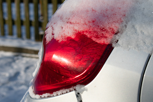 The brake light of the car in the snow. The reflection of the sun. Close up
