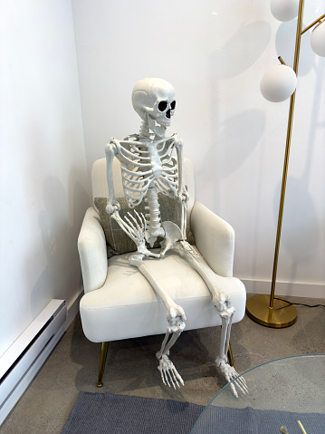 Halloween decoration skeleton sitting on an armchair in a lobby of a residential building