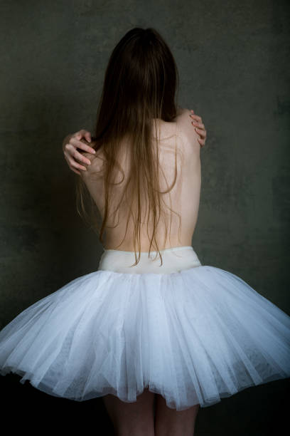 Wide shot of female ballerina sitting and tying her ballet shoes on the floor of a dance studio