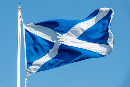 Scottish flag (Saint Andrews flag) on a pole waving on blue sky background