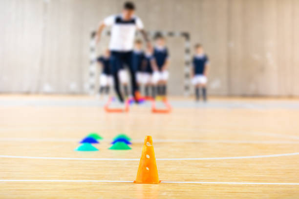 Young coach coaching children during indoor soccer training. Futsal training drills. Indoor soccer equipment. School children during physical education class. PE lesson training equipment tools
