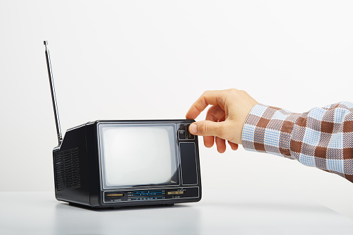 Unrecognizable person changing the channels on old vintage television on white. Hand touching the retro portable tv receiver button