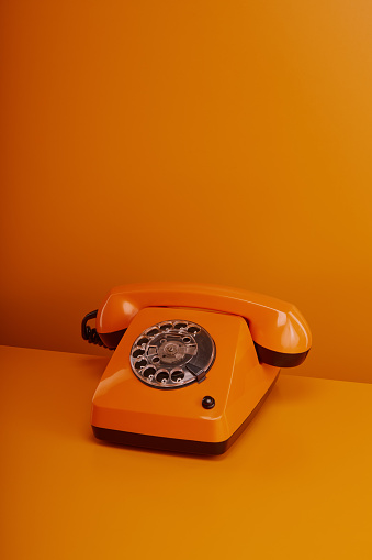 Old fashioned orange vintage telephone. Orange retro phone on orange background