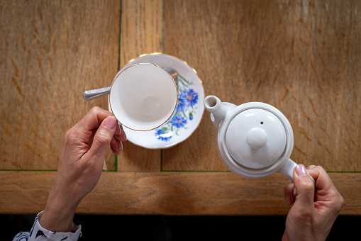 An overhead view of an unrecognisable person ready to pour freshly brewed tea out of a teapot. The rustic cafe is located in Durham, England.