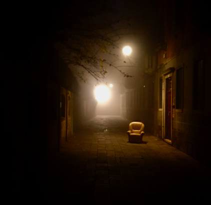 On a foggy night in Venice, a lone chair is found in the middle of a Calle.