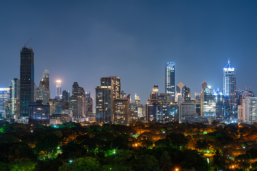 View of night Bangkok city panorama with glowing skyscrapers windows and trees. Concept of tourism and travel in Thailand