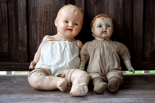 Two worn old dolls sitting on a wooden bench