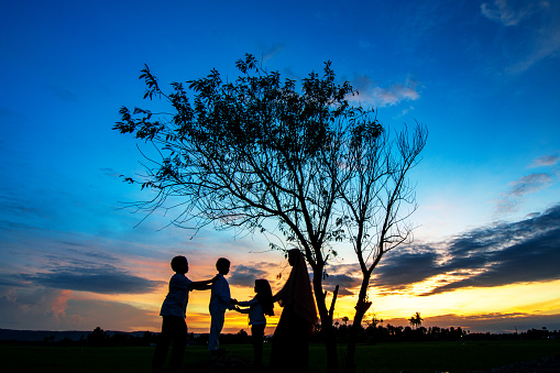 a complete family of 3 children standing under a tree looking at the beautiful sunrise