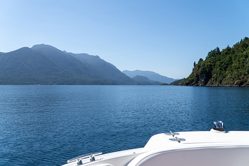 Scenic view from a boat on the calm waters of Lake Panguipulli, surrounded by majestic mountains, creating a tranquil and picturesque landscape.