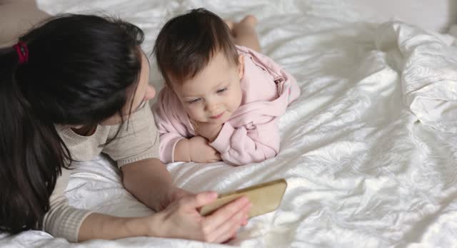 Mother and child playing with smartphone on bed in bedroom at home