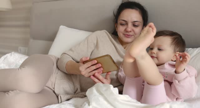 Mother and child playing with smartphone on bed in bedroom at home