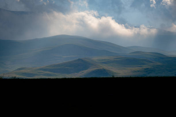 Cloudy weather at high altitudes, wide valley. Mountainous region. Green meadows. Nature view. Light filtering through clouds in the distance.