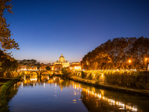 A view of Rome after sunset in autumn, with Ponte Sant'Angelo reflected in the water of the Tiber River.