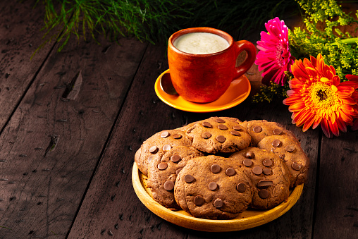 Close up dark coffee in white cup with chocolate chunk crispy cookies on plywood table