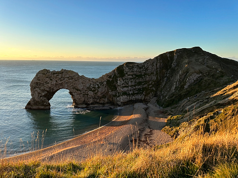 The sun goes down on the Jurassic coast and Durdle Door in Dorset with Seak Pink Trift growing on the top of the cliff in the foreground. Durdle Door, Dorset, Jurassic Coast, England, UK