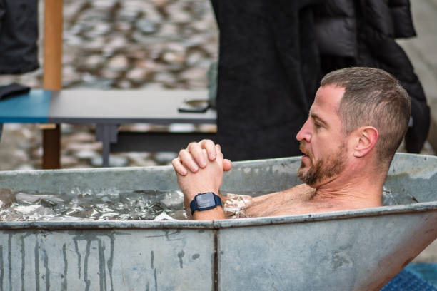 Vilnius, Lithuania - January 28 2024: Handsome boy ice bathing in the cold water among ice cubes in a vintage bathtub. Wim Hof Method, cold therapy, breathing techniques, meditation