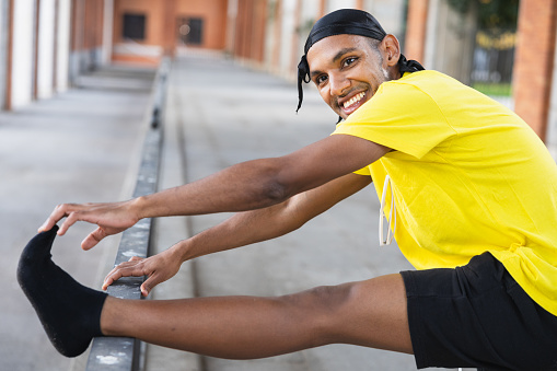 Joyful urban dancer stretching his leg on a handrail, preparing for a dance routine outdoors.