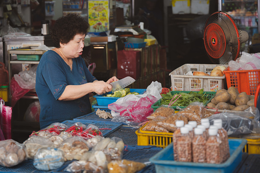 Yilan, Republic of China - October 2, 2023: A shopkeeper chopping broccoli and preparing food at a colourful day market in the city of Yilan, Taiwan.