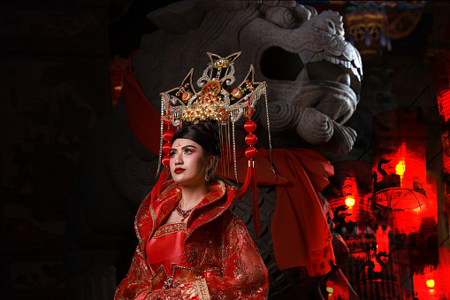 A charming Asian woman in Red ancient Chinese costume with a lion statue at a shrine
