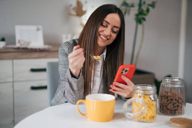 istock Business woman eating breakfast while using her mobile phone 1970619997