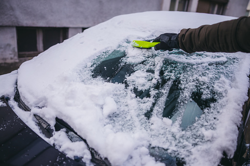 Young man removing snow from the windshield of the car.