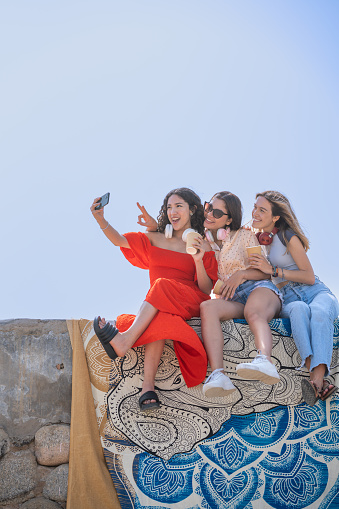 Friends taking a funny selfie with the cell phone sitting on a stone wall stone wall