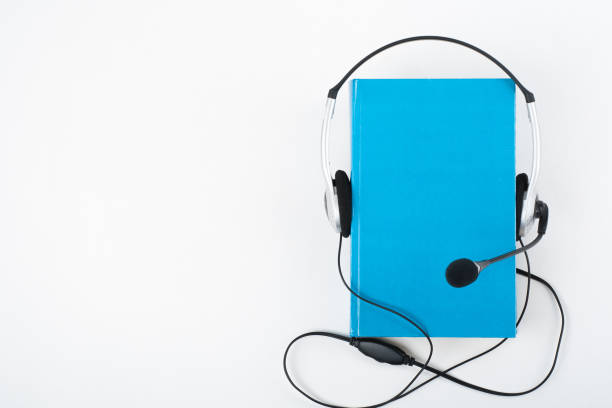 istock Audiobook on white background. Headphones put over blue hardback book, empty cover, copy space for ad text. Distance education, e-learning concept. Top view 1970662477