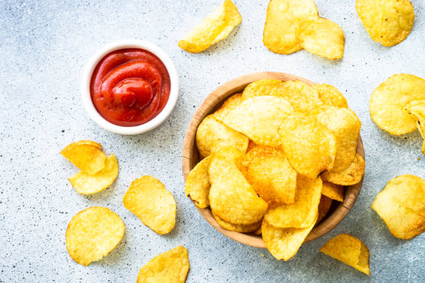 istock Potato chips in wooden bowl on white table. Top view. 1970662987