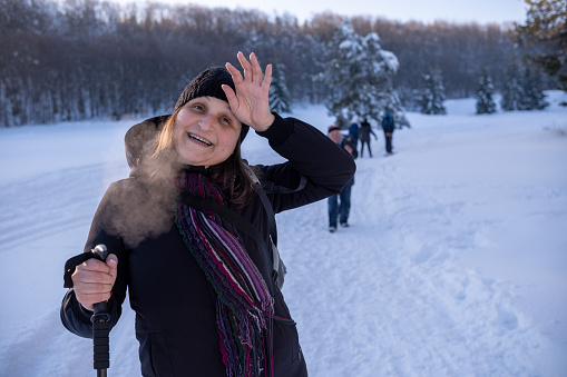 Young cheerful woman in snowy mountain - ski resort. Unrecognizable people walking in the background.