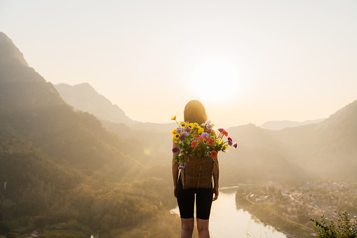 Cheerful woman  with basket full of flowers standing on the background of river in mountains