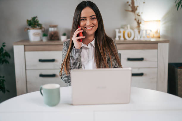 istock A woman is talking on the phone while sitting at a table with a laptop computer 1970668577