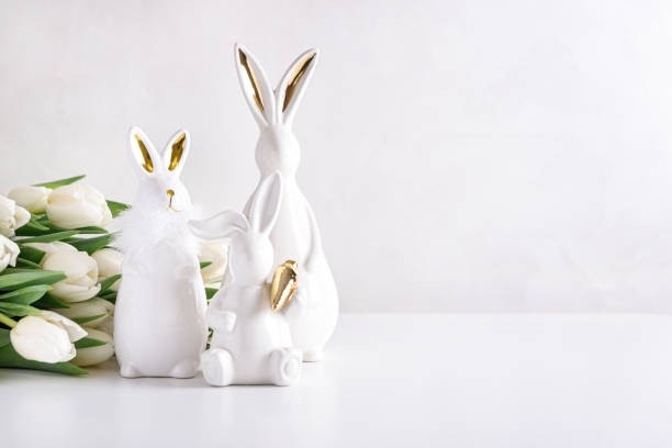 istock Three Easter rabbits figurines with bouquet of white tulips on white background. Easter celebration concept. Copy space. Front view 1970671914