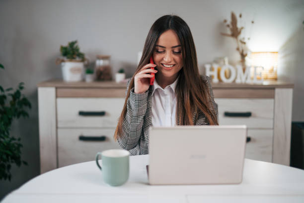 istock A woman is talking on the phone while sitting at a table with a laptop computer 1970673508