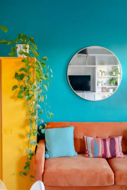 Partial view of a living room designed with vibrant colors, jade wall, coral sofa and yellow bookcase.