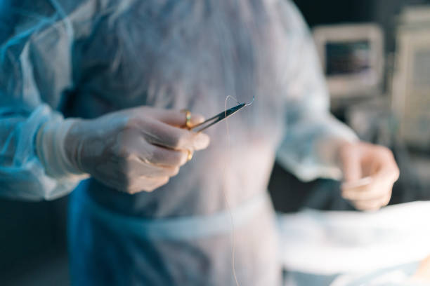 Close-up cropped shot of unrecognizable professional surgeon in uniform holding forceps with suture thread on blurred background Close-up cropped shot of unrecognizable professional surgeon in uniform holding forceps with suture thread on blurred background. Surgeon holding surgical thread with needle holder during operation. stitches wound surgery nurse stock pictures, royalty-free photos & images