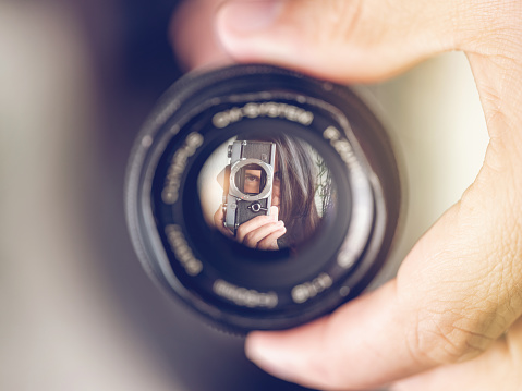 Closeup of crop hand of unrecognizable man holding lens with reflection of woman with retro film photo camera against blurred background