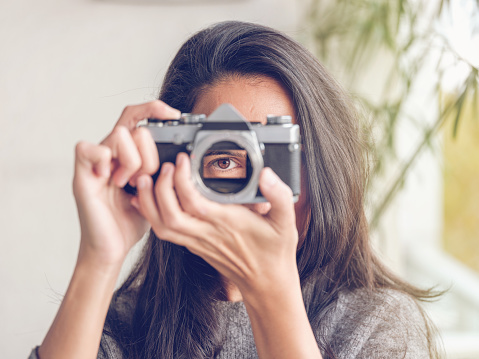 Unrecognizable brunette looking through hole for lens of vintage analog photo camera while pretending to taking photo and looking at camera