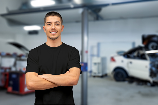 Car mechanic poses with his arms crossed in front of his auto repair shop