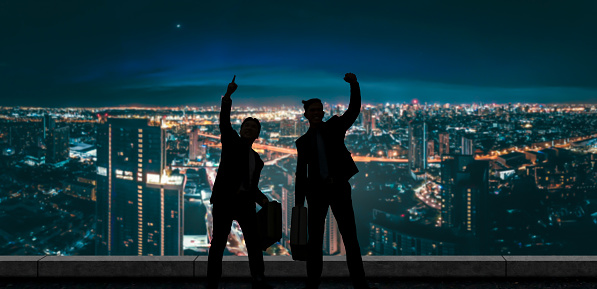 Two joyful businessmen celebrate with a night cityscape backdrop, symbolizing business success and achievement.