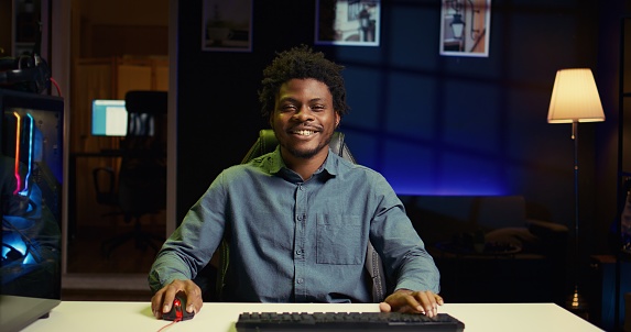 BIPOC man using gaming keyboard to play videogames at home, focused on winning. Gamer using neon lit PC and computer peripherals to compete in internet multiplayer game competition