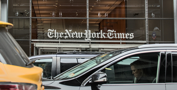 New York, NY - Jan 27, 2023: Cars and taxi cabs drive in front of The New York Times newspaper company sign above the entrance to their corporate headquarters in Times Square, Manhattan, NYC.