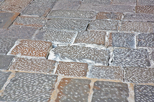 Old and damaged paving made with chiseled sandstone blocks in a pedestrian zone - The surface part is being damaged due to the passage of vehicles