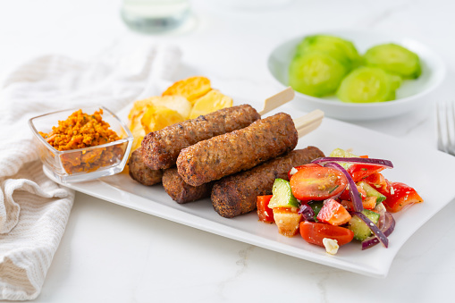 Traditional south european skinless sausages cevapcici made of ground meat with baked potatoes and small salad and dip.